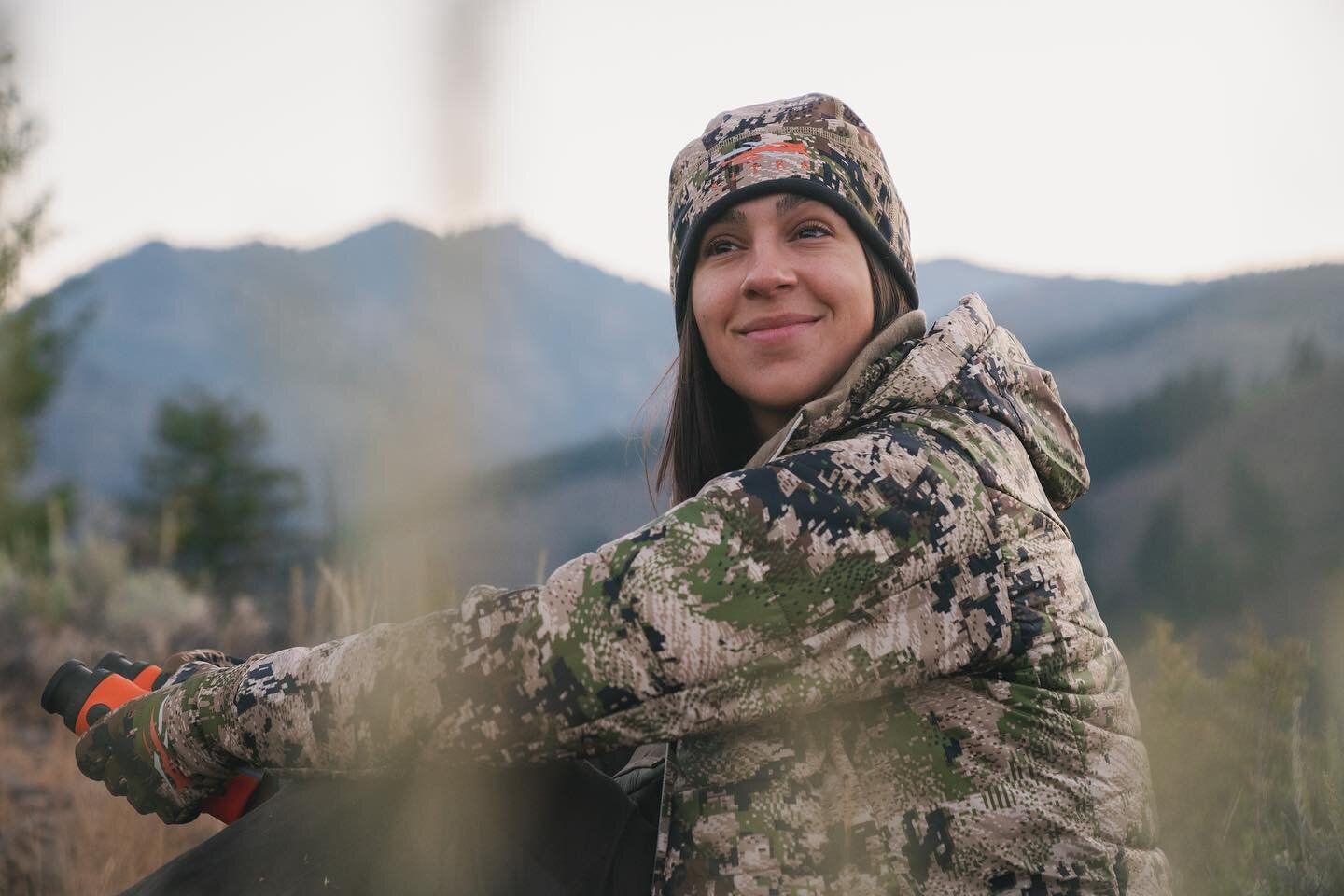 Alli D/Andrea in camo with binoculars outdoors. 