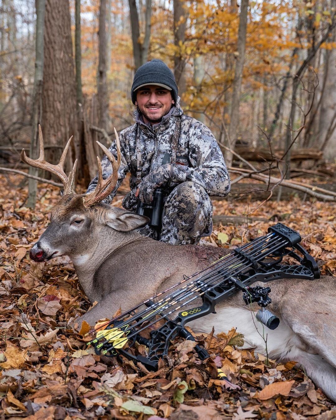 Chris Bee with a deer kill and a bow laying on the deer. 