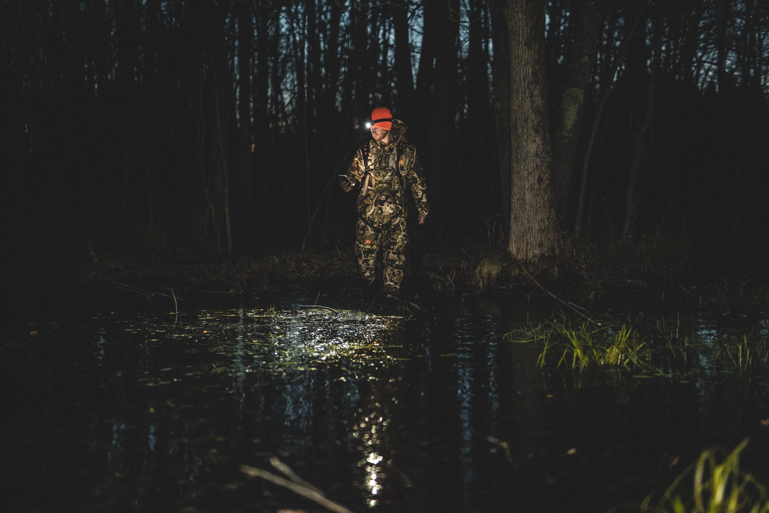 A hunter using a headlamp and the HuntWise app on a phone while scouting before opening day. 