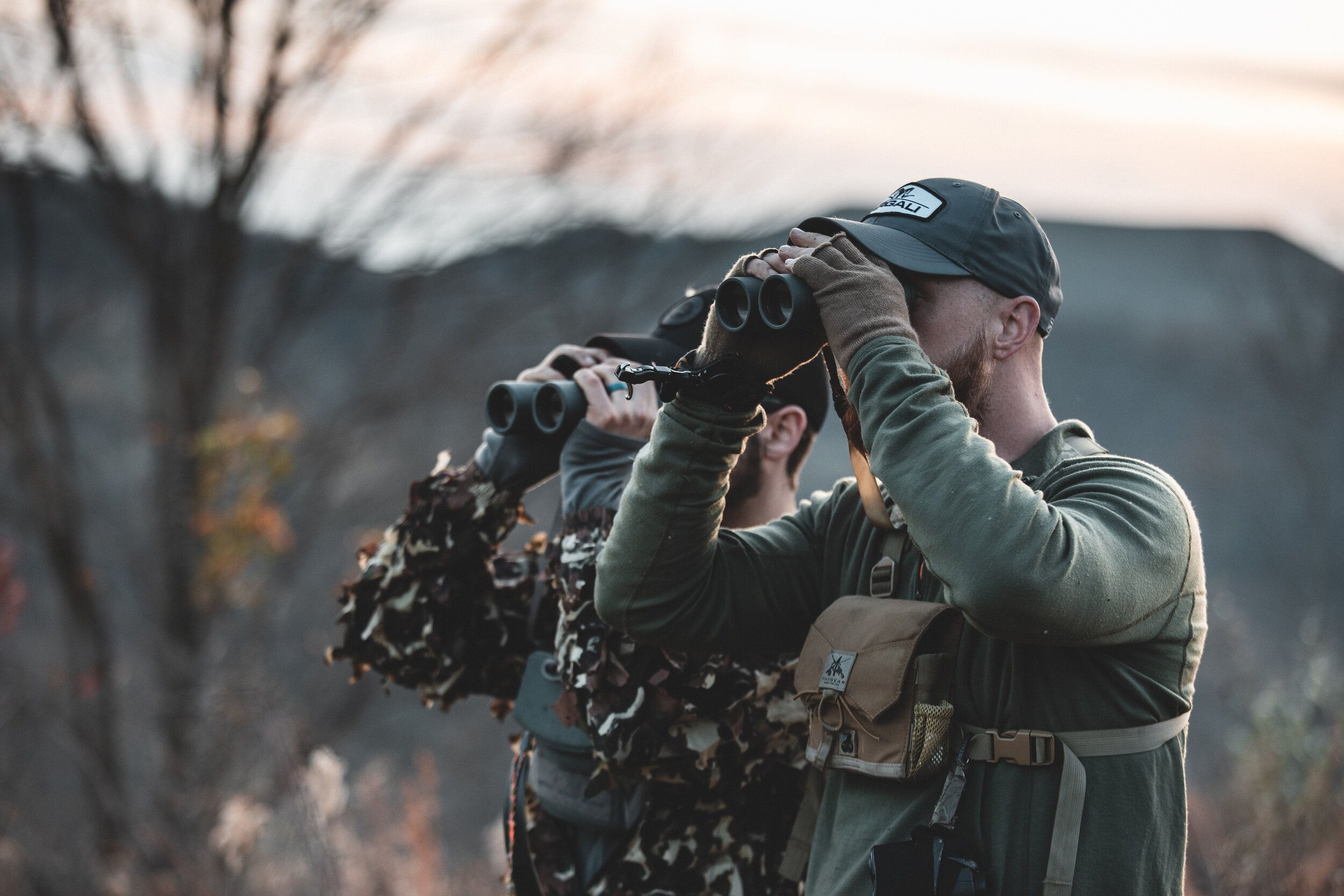 Two members of Bowga hunting outdoors using binoculars. 