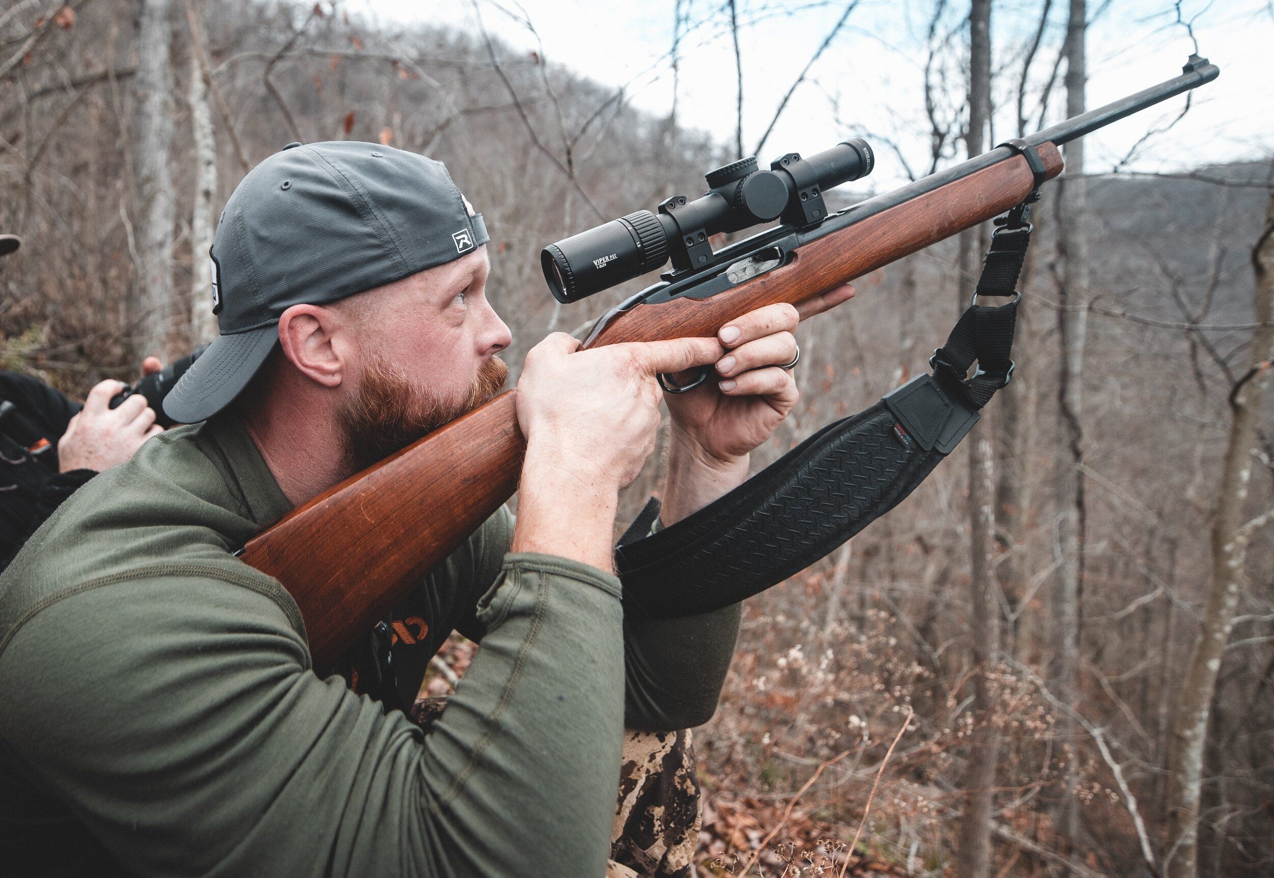 A hunter points a rifle into a tree, squirrel hunting tips. 