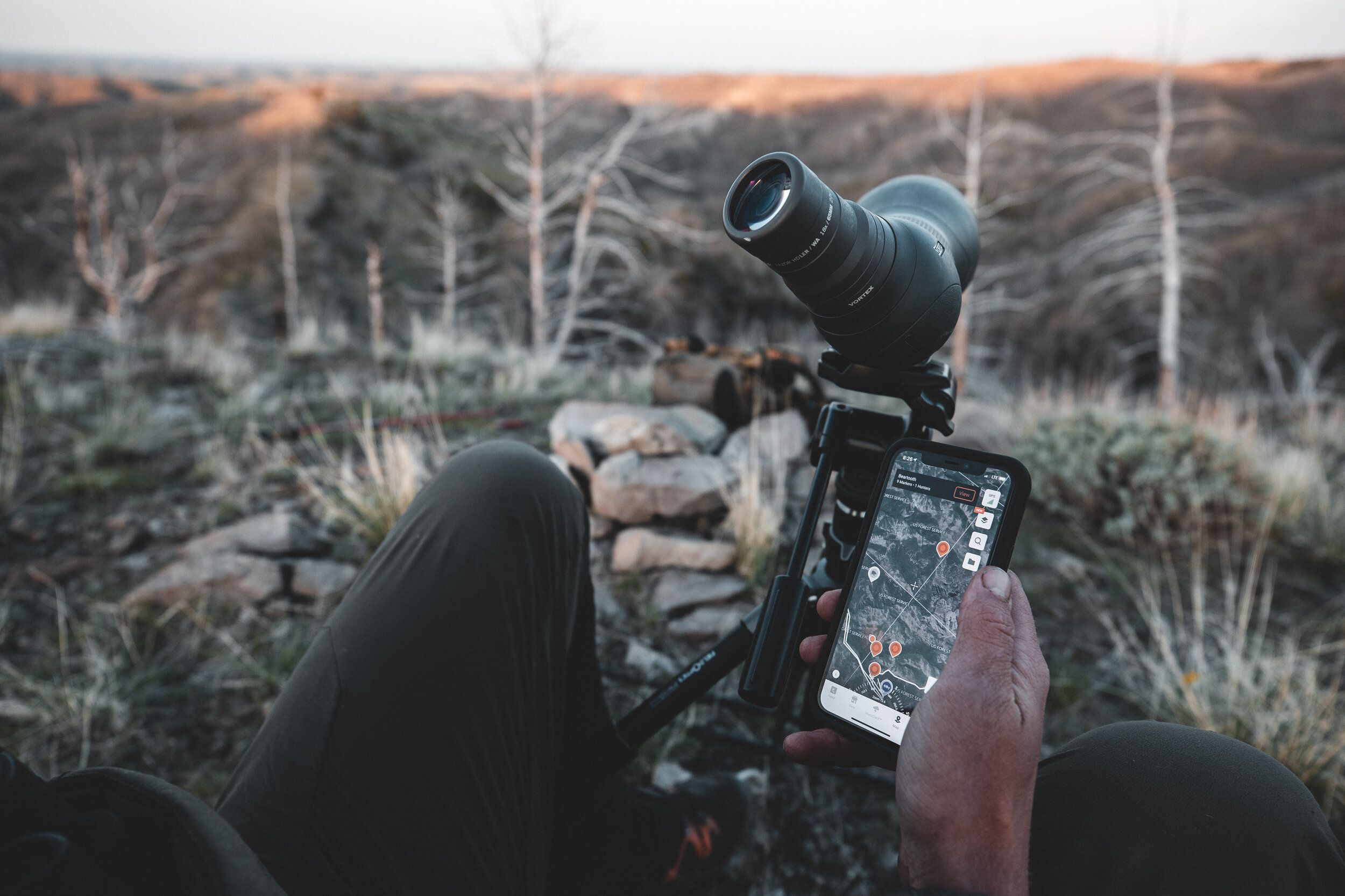 Close-up of a scope and a hand holding a phone with HuntWise on screen, glassing while western hunting concept. 