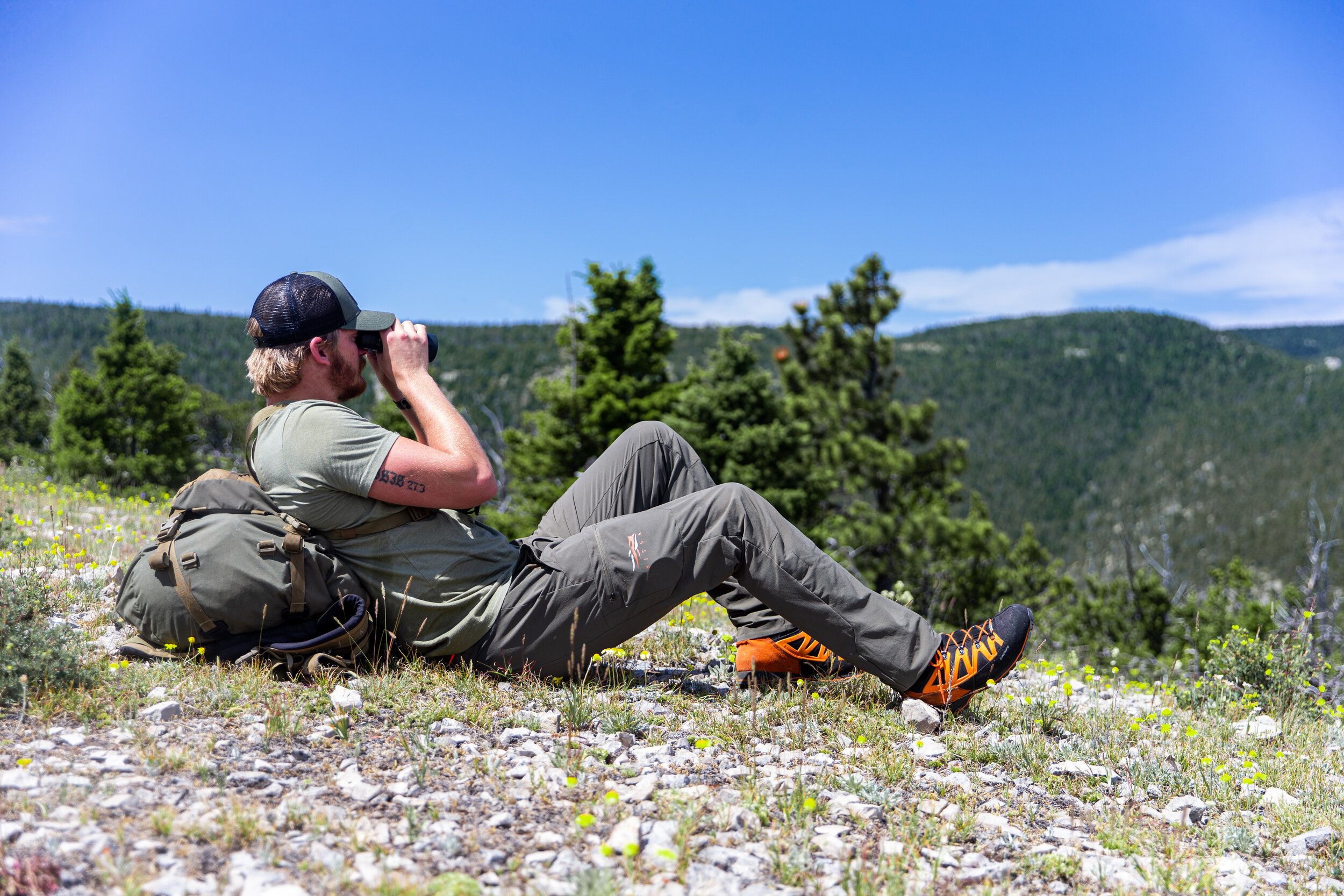 A hunter lies on the ground using binoculars, scout for elk concept. 