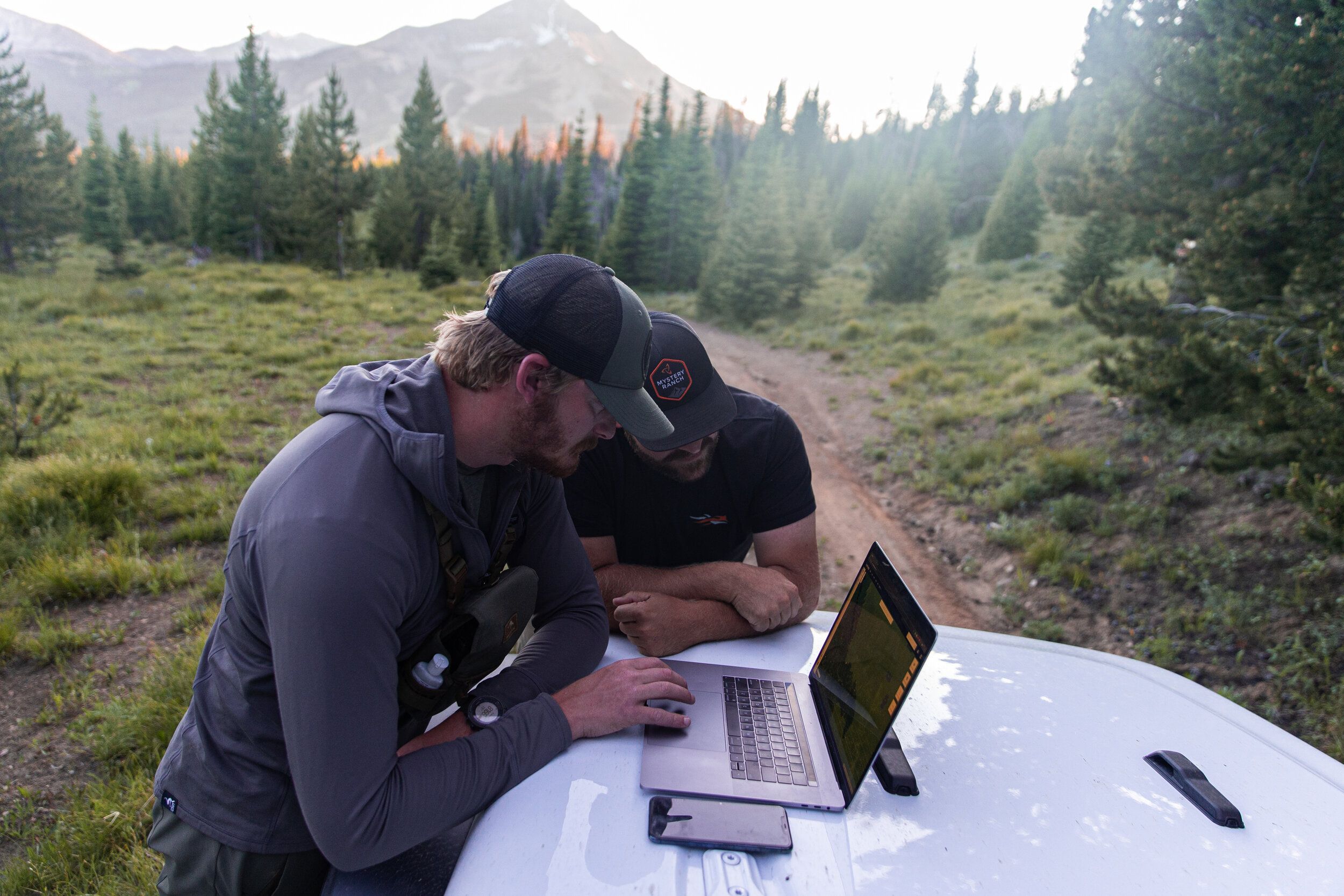 Two hunters look at a laptop sitting on a truck's hood, e-scouting for elk concept. 