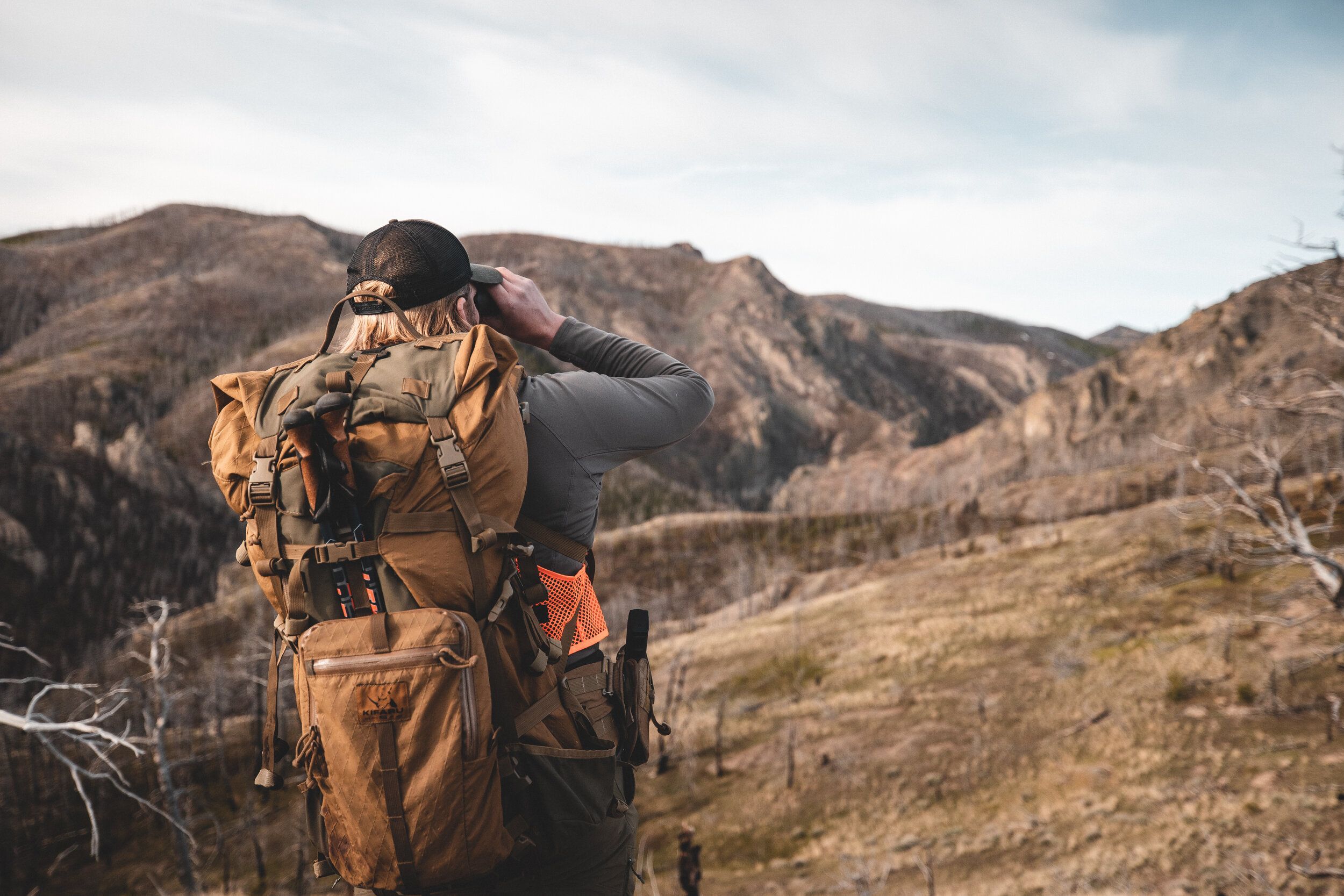 A hunter wearing a backpack looks through binoculars, western hunting concept. 