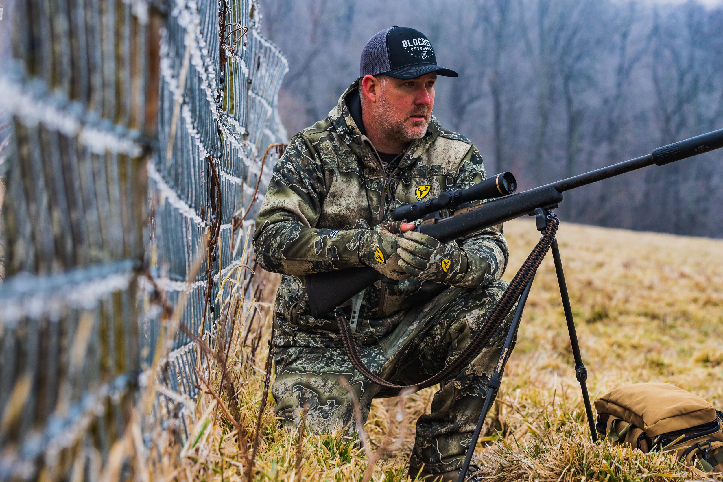 Jon Collins kneels in a field with a rifle.