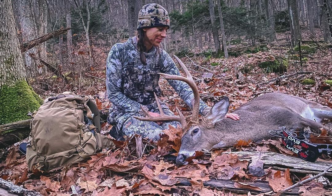 Allie D'Andrea sits on the ground with her deer kill after using the hunting app HuntWise. 