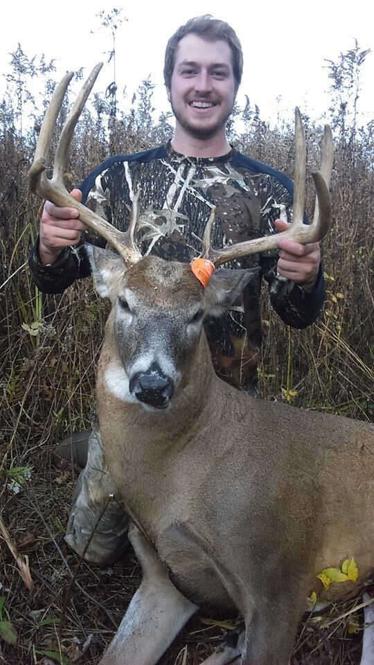 A smiling hunter holding the head and antlers of a big buck in the field, how to find bucks on public land concept. 