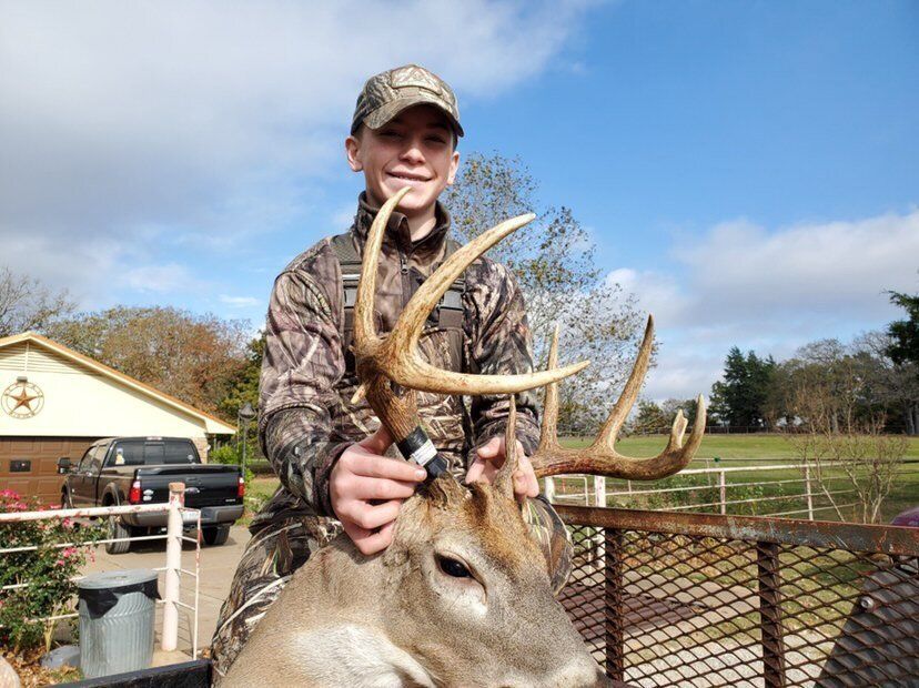 A boy in camo smiles and holds up a deer head and antlers, 2020 hunting success concept. 