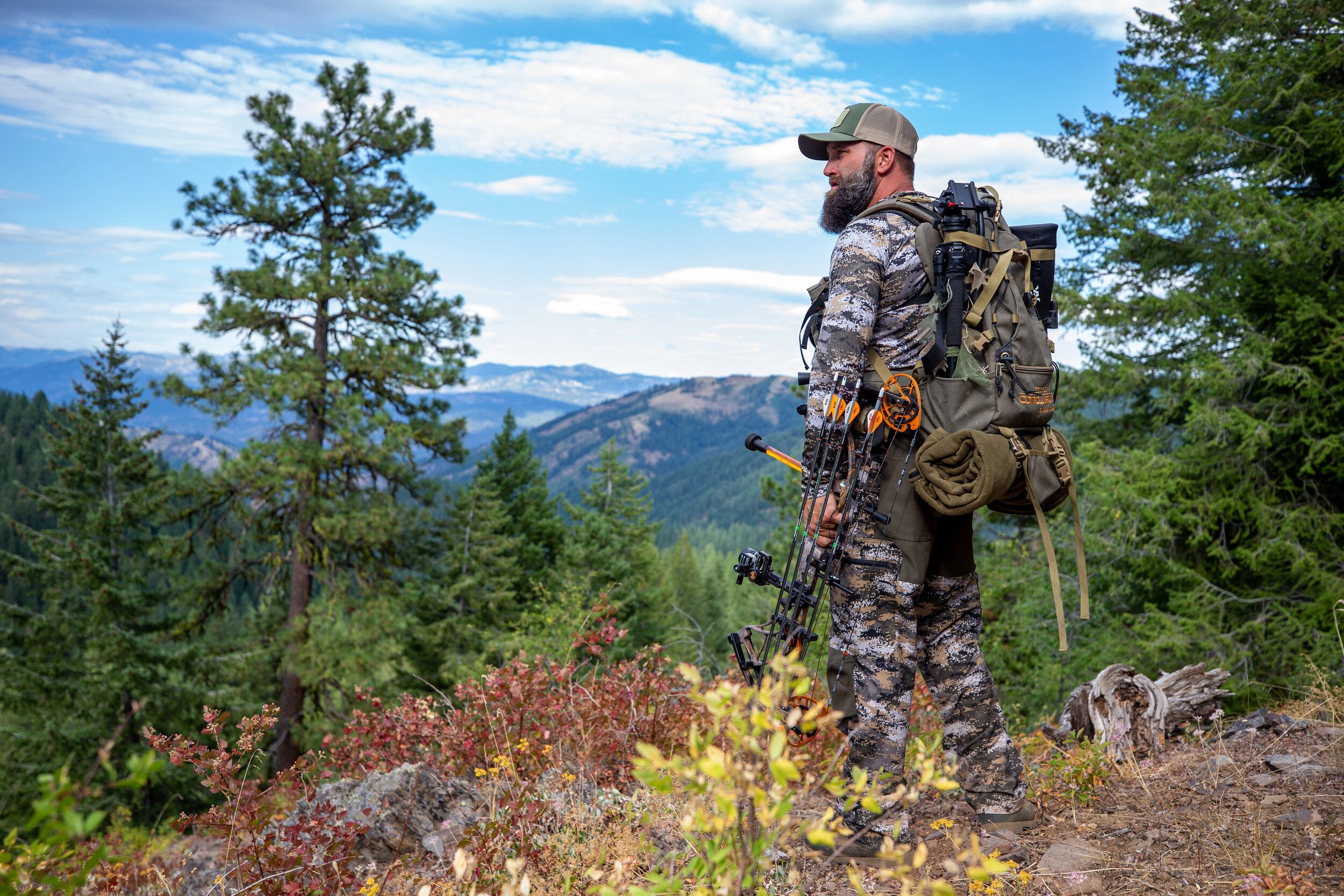 A hunter stands on a ridge with a bow, elk hunting concept. 