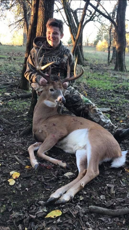 A boy smiles and holds up a deer after the kill, using the HuntWise app concept. 